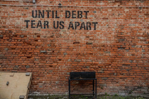 The phrase 'until debt tear us apart' written on a red brick wall